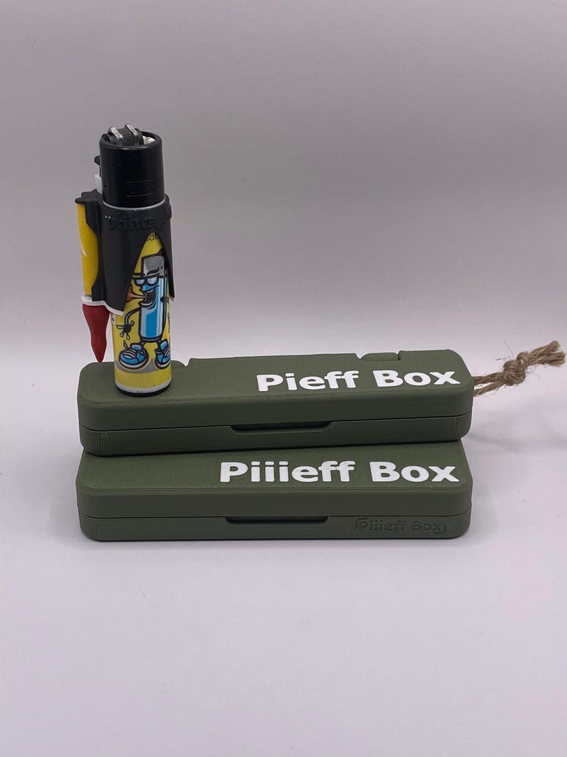 Pu&ograve; includere: Due scatole verdi con il testo "Pieff Box" e "Pilieff Box" stampato in bianco sul davanti. Un accendino nero con un personaggio dei cartoni animati sopra &egrave; seduto sopra le scatole.
