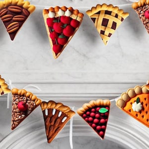 May include: A festive garland of felt pie slices in various flavors, including cherry, pecan, and pumpkin. The garland is strung together with white twine and would be a fun addition to a Thanksgiving or fall-themed party.