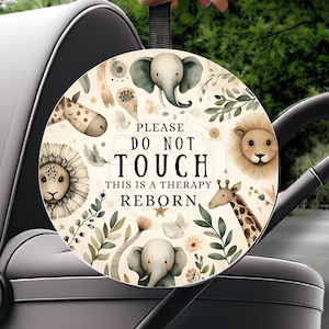 Può includere: Un cerchio decorativo per passeggino con illustrazioni di animali della savana ad acquerello. Il cerchio presenta la scritta "PLEASE DO NOT TOUCH THIS IS A THERAPY REBORN". Il design include elefanti, giraffe e leoni.