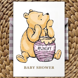 May include: A greeting card with a watercolour illustration of a yellow bear holding a pink striped honey pot with the word "HUNNY". The words "BABY SHOWER" are printed in brown below the bear.
