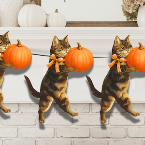 May include: A garland featuring paper cats holding orange pumpkins, each adorned with an orange bow. The cats are brown and tan with black stripes. The garland is strung on a black string, ideal for Halloween or autumn decorations.