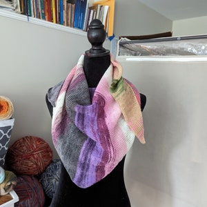 May include: A triangular scarf with a pink, purple, gray, and beige color gradient. The scarf is draped over a black mannequin.