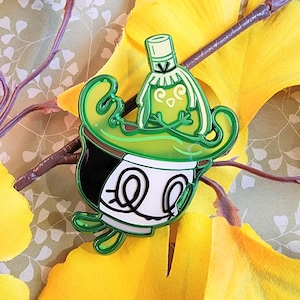 Puede incluir: Pin de esmalte verde y blanco con un personaje de dibujos animados con un sombrero verde y una cara verde y blanca. El personaje lleva un sombrero verde y blanco con un borde blanco y una cara verde y blanca con una nariz blanca y ojos. El personaje sostiene una taza verde y blanca con una tapa verde y blanca.