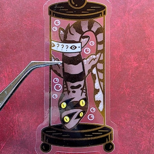 May include: A clear sticker featuring a cartoon creature inside a glass jar. The creature has yellow eyes and a striped body, wearing a mask with question marks. The jar is on a black base with a round top.