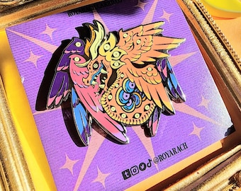 May include: A colorful enamel pin featuring a winged creature with multiple eyes, in shades of pink, orange, purple, and blue. The pin is set on a purple card with starburst designs and the text "ROYARACH". The pin is displayed in a gold frame.