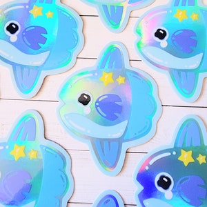 May include: A set of iridescent blue and purple fish stickers with a star design. The fish have a tear-drop shape and a fin on the top of their head. The stickers are perfect for adding a touch of whimsy to any project.