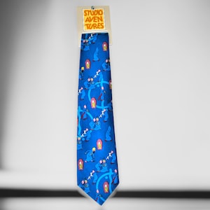 Könnte beinhalten: Eine blaue Seidenkrawatte mit einem sich wiederholenden Muster aus Comicfiguren in Blau, Rosa und Gelb. Die Krawatte hat ein Etikett mit der Aufschrift "Studio Adventures".