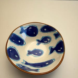 May include: A ceramic bowl with a white interior and a brown rim. The bowl is decorated with blue fish designs. The fish vary in shape and size, adding a whimsical touch to the piece. The bowl is likely used for serving food.
