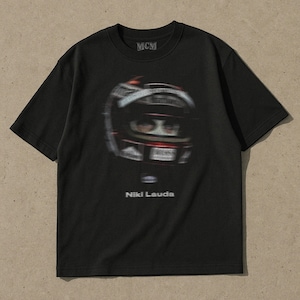 May include: Black t-shirt featuring a graphic of a racing driver wearing a helmet. The text "MCM" and "Niki Lauda" is printed on the shirt.