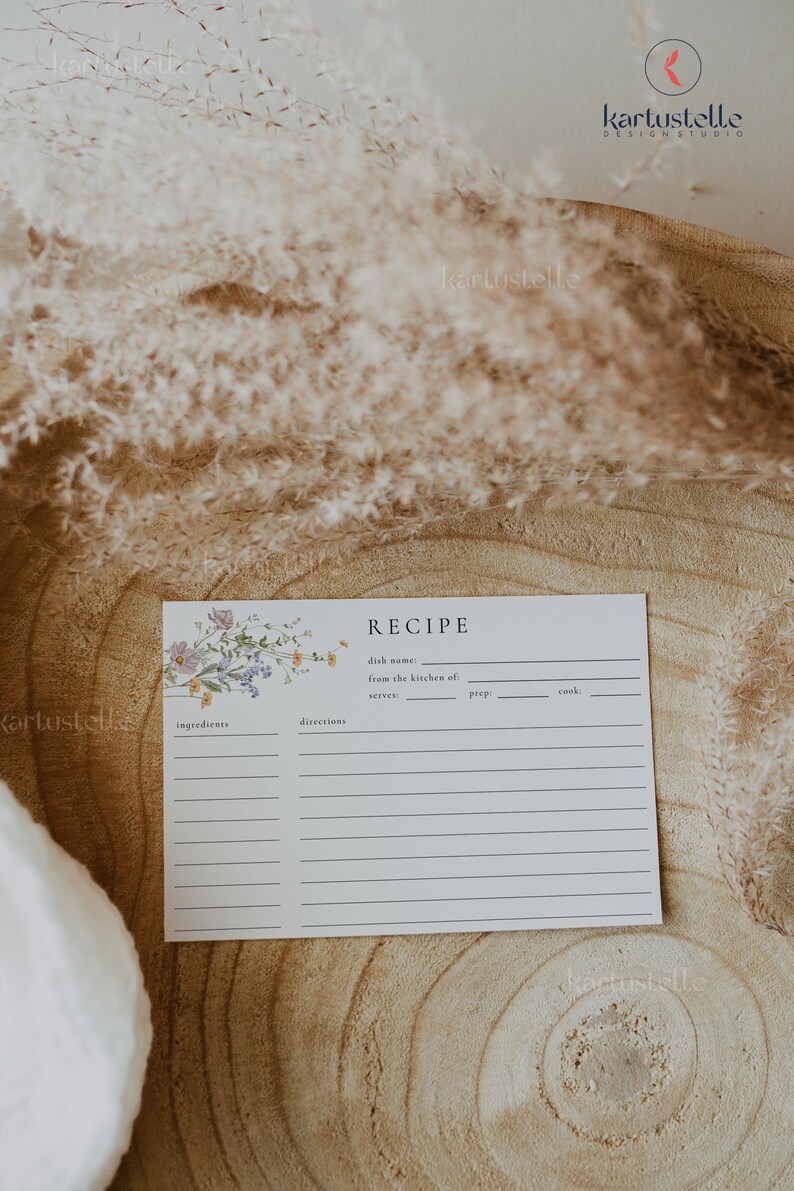 May include: A white recipe card with floral accents and the word "RECIPE" at the top. The card includes spaces for ingredients, directions, and other details. The background features dried plants and a wooden surface.