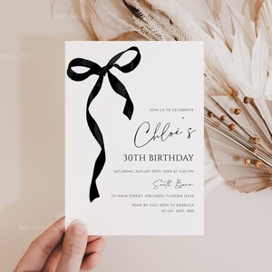 K&ouml;nnte beinhalten: Eine wei&szlig;e Geburtstagseinladungskarte mit einem schwarzen Schleifendesign und dem Text "Chloe's 30. Geburtstag". Die Karte enth&auml;lt Veranstaltungsdetails. Die Einladung wird von einer Hand gehalten.