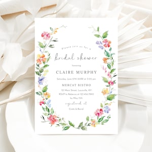 Puede incluir: Una corona de flores de acuarela rodea una invitaci&oacute;n a una despedida de soltera para Claire Murphy. La invitaci&oacute;n incluye la fecha, la hora, el lugar y la informaci&oacute;n de RSVP. El texto dice "Por favor, &uacute;nase a nosotros para una despedida de soltera en honor a Claire Murphy, s&aacute;bado 27 de junio de 20XX a las 3:00 pm, Mercat Bistro, 121 Main Street, Louisville, KY, RSVP a Rebecca al 123.456.7890 antes del 15 de mayo, registrado en Crate & Barrel."