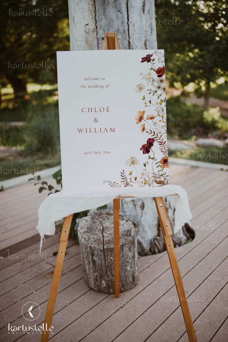 May include: A white wedding welcome sign with a floral design featuring burgundy, orange, and yellow flowers. The sign reads "Welcome to the wedding of Chloe & William, April 26th, 20xx".