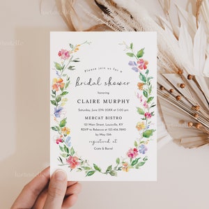 Puede incluir: Una invitaci&oacute;n a una despedida de soltera floral con una corona de acuarela de flores rosas, amarillas, azules y naranjas. El texto de la invitaci&oacute;n dice: "Por favor, &uacute;nase a nosotros para una despedida de soltera en honor a Claire Murphy S&aacute;bado, 27 de junio de 20XX a las 3:00 pm Mercat Bistro 121 Main Street, Louisville, KY RSVP a Rebecca al 123.456.7890 antes del 15 de mayo registrado en Crate & Barrel"