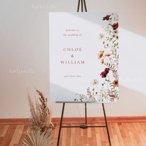 May include: A white wedding welcome sign with a floral design in shades of brown, orange, and red. The sign reads "Welcome to the wedding of Chloe & William, April 26th, 20xx".