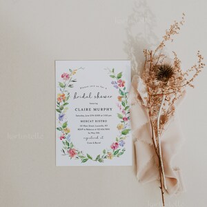 Puede incluir: Una invitaci&oacute;n de ducha nupcial floral con una corona de acuarela de flores rosas, amarillas y azules. La invitaci&oacute;n es para Claire Murphy e incluye la fecha, la hora, la ubicaci&oacute;n y la informaci&oacute;n de RSVP. El texto dice "Por favor, &uacute;nase a nosotros para una bridal shower en honor a Claire Murphy S&aacute;bado, 27 de junio de 20XX a las 3:00 pm Mercat Bistro 121 Main Street, Louisville, KY RSVP a Rebecca al 123.456.7890 antes del 15 de mayo registrado en Crate & Barrel"