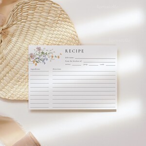 May include: A recipe card with floral accents and the word "RECIPE" at the top. The card has lines for ingredients, directions, and other details. A woven fan and ribbon are in the background.