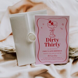 Puede incluir: Una invitaci&oacute;n rosa con una ilustraci&oacute;n de c&oacute;ctel y el texto "Dirty Thirty" para el 30 cumplea&ntilde;os de Emily. Incluye un sobre con un sello de cera. La invitaci&oacute;n est&aacute; sobre una tela color crema.