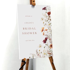 Może przedstawiać: Biały znak z kwiatowym wzorem w odcieniach czerwieni, pomarańczy i brązu. Na znaku widnieje napis "Witamy na Bridal Shower Chloe, 26 kwietnia 20xx".