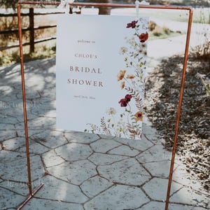 Może przedstawiać: Biały znak z kwiatowym wzorem i tekstem "welcome to CHLOE'S BRIDAL SHOWER april 26th, 20xx" jest wyświetlany na stojaku z rur miedzianych.