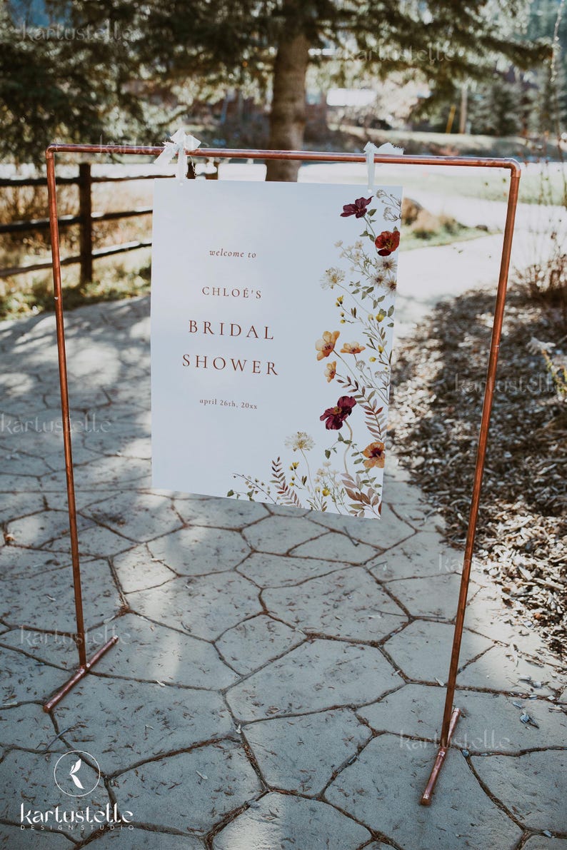 Może przedstawiać: Biały znak z kwiatowym wzorem i tekstem "welcome to CHLOE'S BRIDAL SHOWER april 26th, 20xx" jest wyświetlany na stojaku z rur miedzianych.