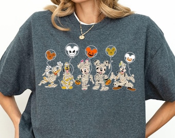May include: Dark heather gray sweatshirt featuring a Halloween-themed graphic. The graphic depicts cartoon characters dressed as mummies, holding balloons. The balloons have Mickey Mouse, Minnie Mouse, and pumpkin designs. The text "Dark Heather" is at the bottom left.