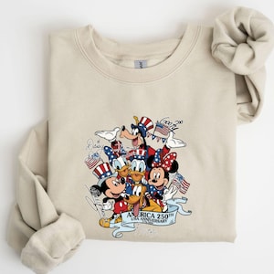 Puede incluir: Sudadera de color arena con un gr&aacute;fico colorido de personajes de Disney, incluyendo Mickey y Minnie Mouse, Goofy y Donald Duck, celebrando el 250 aniversario de Am&eacute;rica. El dise&ntilde;o incorpora elementos patri&oacute;ticos como banderas y sombreros del T&iacute;o Sam.