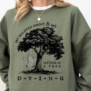 May include: A green sweatshirt with a black graphic print of a ghost and a tree. The text on the graphic reads "My Beloved Ghost & Me Sitting In A Tree D-Y-I-N-G".