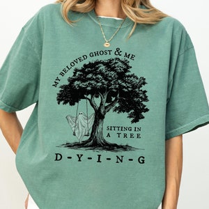 May include: A green t-shirt with a black graphic of a ghost sitting in a tree with the text "My Beloved Ghost & Me" and "Sitting in a Tree" and "D-Y-I-N-G".