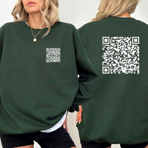 May include: A dark green sweatshirt with a white QR code printed on the front and back. The sweatshirt has a crew neck and long sleeves. The model is wearing black shorts and a white undershirt.
