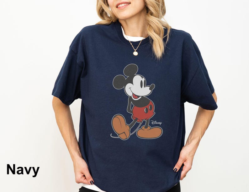 May include: Navy blue t-shirt featuring a classic Mickey Mouse graphic. The cartoon character is depicted in his iconic pose, wearing red shorts and brown shoes. The word "Disney" is printed below the character. The word "Navy" is printed in the bottom left corner.