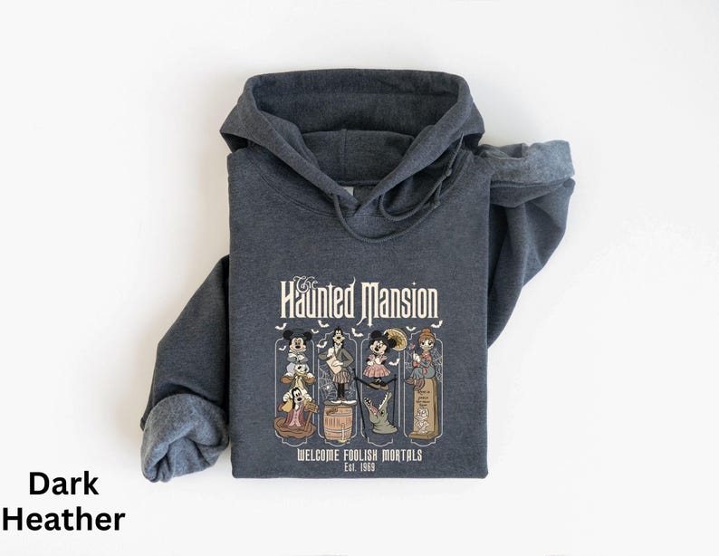 May include: Dark heather gray hooded sweatshirt featuring a graphic from The Haunted Mansion. The graphic includes cartoon characters and the text "The Haunted Mansion Welcome Foolish Mortals Est. 1969."