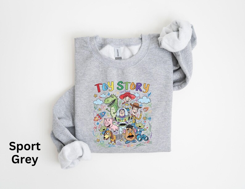 May include: Sport grey sweatshirt featuring a colorful graphic of Toy Story characters, including Woody, Buzz Lightyear, and Rex. The words "Toy Story" are written above the characters in a playful font. The sweatshirt has a crew neck and long sleeves.
