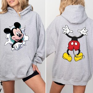 May include: Sport Grey hoodie featuring Mickey Mouse. The front shows Mickey breaking through a torn hole, while the back displays Mickey's backside. The hoodie has a front pocket and a hood.