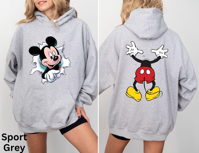 May include: Sport Grey hoodie featuring Mickey Mouse. The front shows Mickey breaking through a torn hole, while the back displays Mickey's backside. The hoodie has a front pocket and a hood.