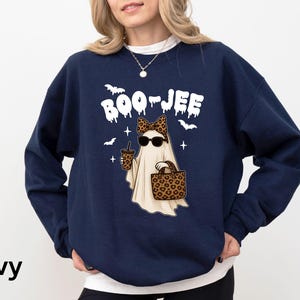 Op de afbeelding: Marineblauwe sweatshirt met een spookafbeelding met een zonnebril en een luipaardstrik, met een drankje en een handtas. De tekst "BOO-JEE" staat boven het spook, met vleermuizen en sterren. Halloween-thema.