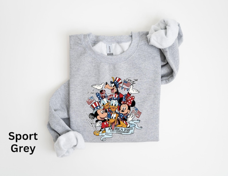 Puede incluir: Sudadera gris deportiva con un dise&ntilde;o de Mickey Mouse, Minnie Mouse, Donald, Goofy y Pluto con atuendos patri&oacute;ticos. El dise&ntilde;o incluye banderas americanas y el texto "AMERICA 250th ANNIVERSARY". La sudadera tiene cuello redondo y mangas largas.