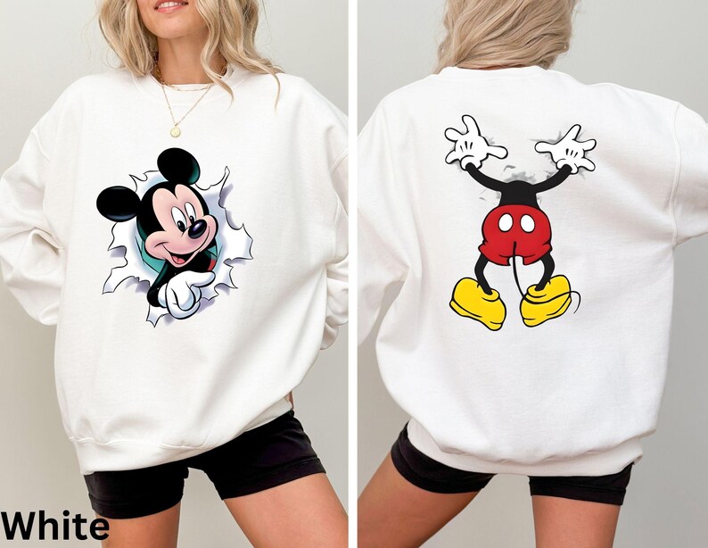 May include: White sweatshirt featuring a Mickey Mouse graphic on the front and back. The front design shows Mickey breaking through a torn-paper effect. The back design depicts Mickey's legs and arms. The word "White" is printed at the bottom.