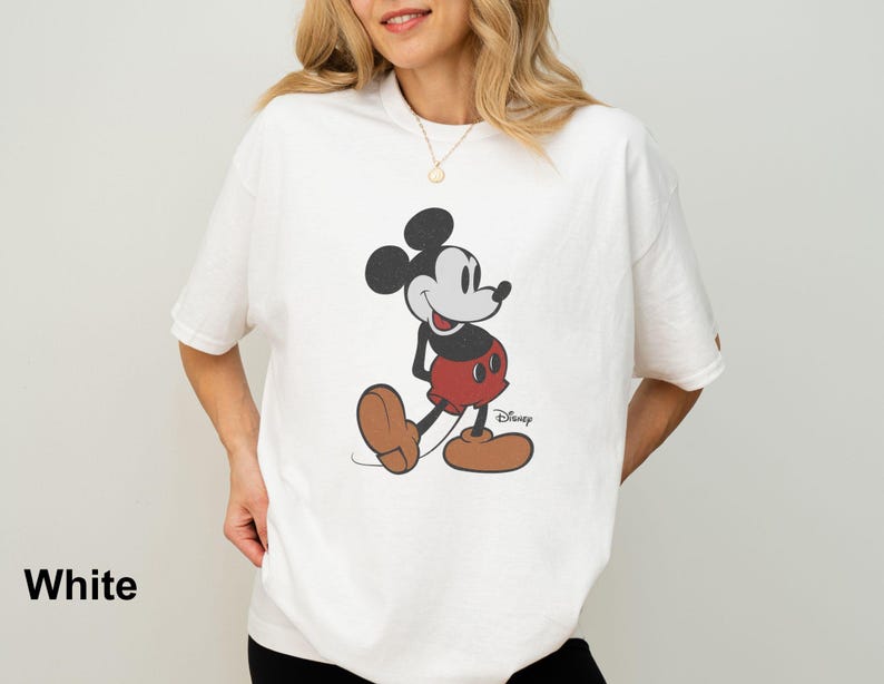 May include: White t-shirt featuring a classic Mickey Mouse graphic. The cartoon character is depicted in black, red, and brown, with the Disney logo visible. The word "White" is printed at the bottom left of the image.