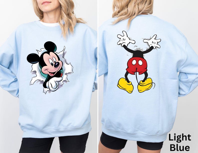 May include: Light blue sweatshirt featuring Mickey Mouse graphics on the front and back. The front graphic shows Mickey breaking through a torn surface, while the back displays Mickey's full body. The text "Light Blue" is visible.