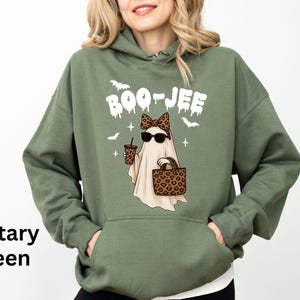 Op de afbeelding: Militairgroene hoodie met een cartoongeest met een zonnebril, een luipaardprint strik, een handtas en een koffiekopje. Boven de geest staat in het wit het woord "BOO-JEE". Het ontwerp bevat ook vleermuizen en kruisen.
