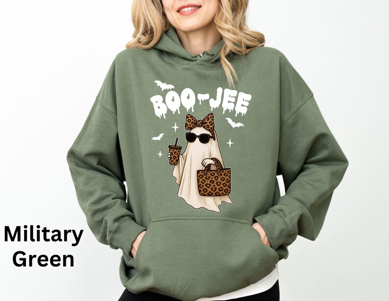 Op de afbeelding: Militairgroene hoodie met een cartoongeest met een zonnebril, een luipaardprint strik, een handtas en een koffiekopje. Boven de geest staat in het wit het woord "BOO-JEE". Het ontwerp bevat ook vleermuizen en kruisen.