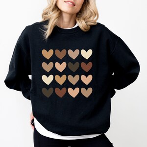 May include: Black sweatshirt with a pattern of 16 different colored hearts. The hearts are arranged in a 4x4 grid.