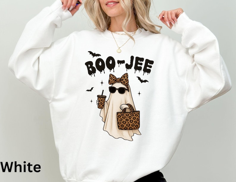 Op de afbeelding: Witte sweatshirt met een Halloween-thema. Het ontwerp toont een spook met een zonnebril en een luipaardprint strik, met een koffiebeker en een handtas. De tekst "BOO-JEE" staat boven het spook.