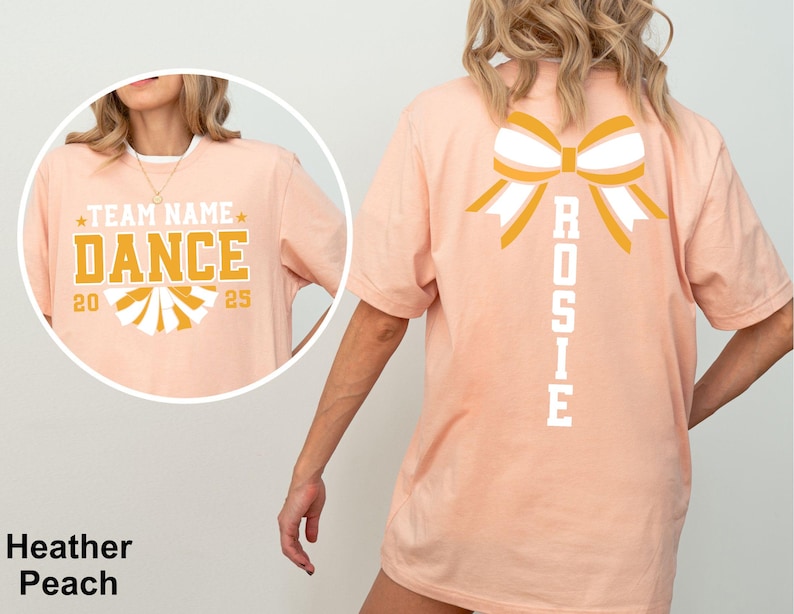 May include: Heather peach t-shirt with a large bow graphic on the back and the name "Rosie" printed vertically. The front features the text "Team Name Dance 2025" in gold and white.