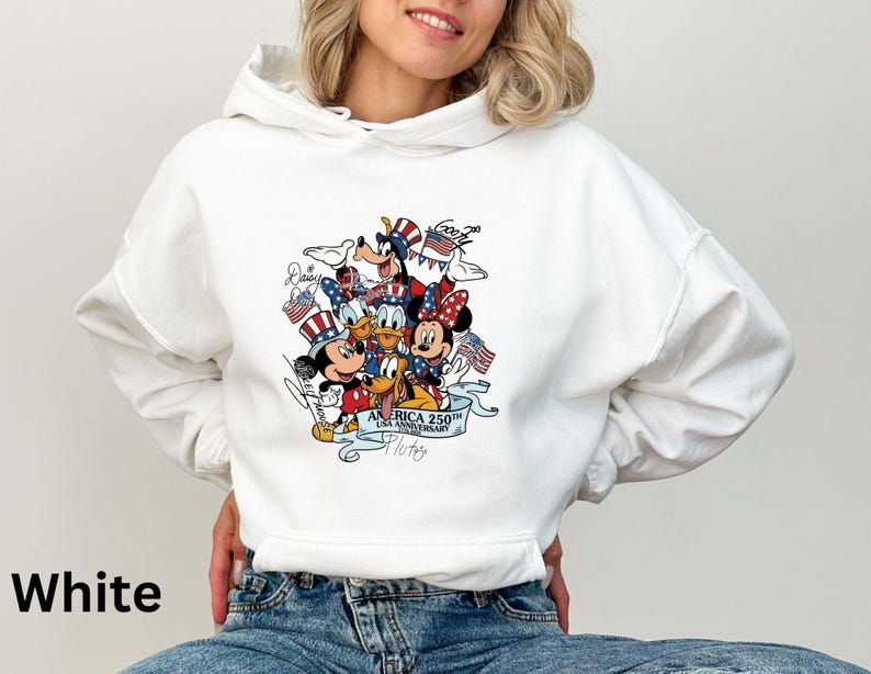 Puede incluir: Sudadera con capucha blanca con un gr&aacute;fico colorido de personajes de Disney, incluyendo Mickey y Minnie Mouse, Donald Duck y Goofy, celebrando el 250 aniversario de EE. UU. El dise&ntilde;o incorpora elementos patri&oacute;ticos como banderas y estrellas.