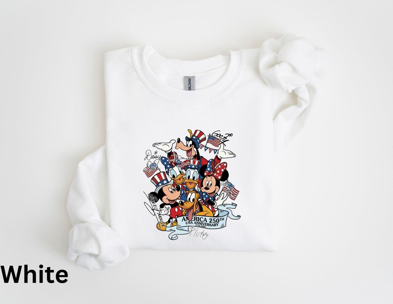 Puede incluir: Sudadera blanca de manga larga con un gr&aacute;fico colorido de personajes de Disney, incluyendo Mickey y Minnie Mouse, Donald Duck y Goofy, celebrando el 250 aniversario de EE. UU. El dise&ntilde;o incorpora elementos patri&oacute;ticos como banderas y estrellas.