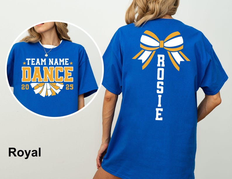 May include: Royal blue t-shirt with a cheerleading design. The front features the text "TEAM NAME DANCE 2025" in gold and white. The back displays a bow graphic and the name "ROSIE" in white.