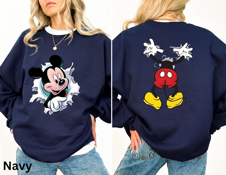 May include: Navy blue sweatshirt featuring a Mickey Mouse graphic. The front shows Mickey breaking through a white-edged hole. The back displays Mickey's full body with outstretched arms. The sweatshirt has a white crew neck.