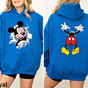 May include: Royal blue hoodie featuring Mickey Mouse. The front of the hoodie shows Mickey breaking through a torn white background. The back of the hoodie displays Mickey's full body, with his arms raised. The hoodie has a front pocket.